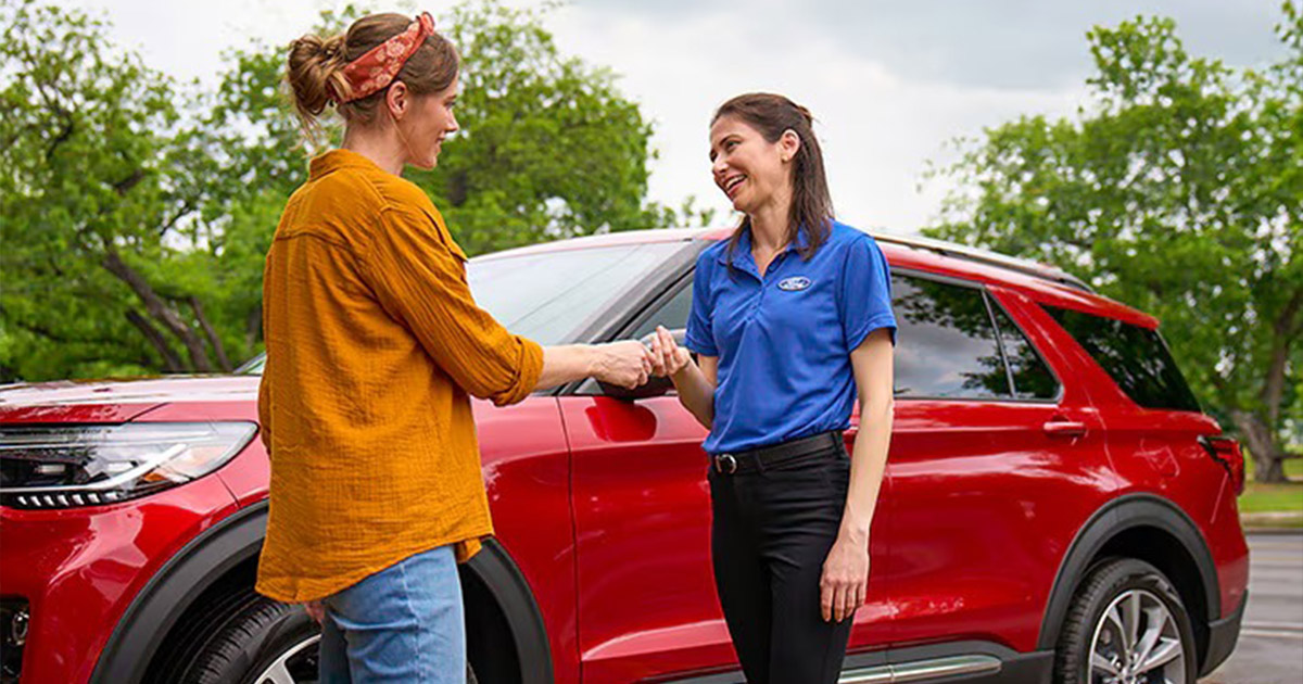 Ford service member greeting a customer in front of a red Ford SUV.