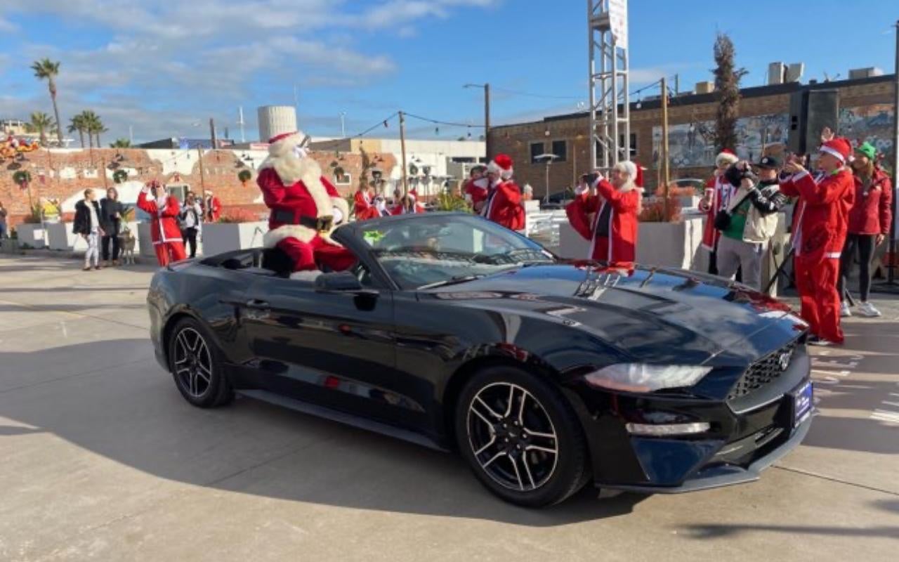 Santa Claus in a black convertible Ford Mustang with a crowd